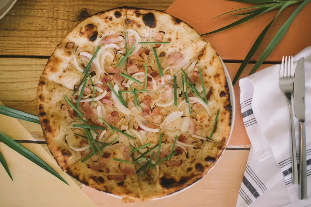 Sliced wood-fired pizza with onions, bacon, and chives.