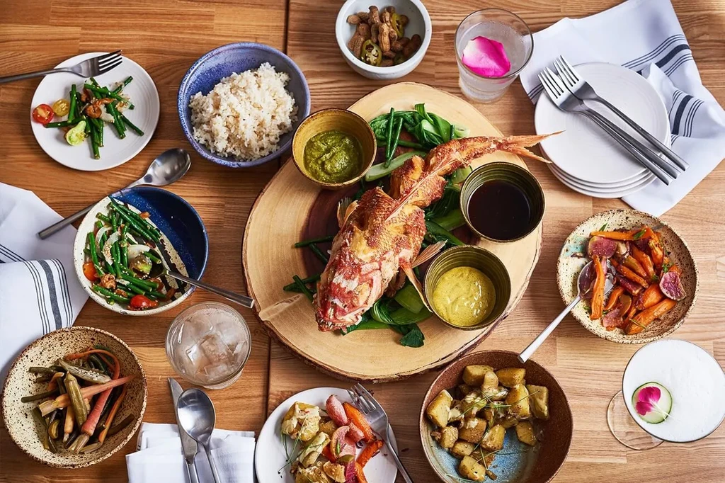 Overhead shot of a styled meal: whole fish, vegetables, rice, and drinks.