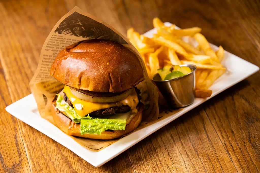Burger, golden french fries, and green dipping sauce on a wooden table.