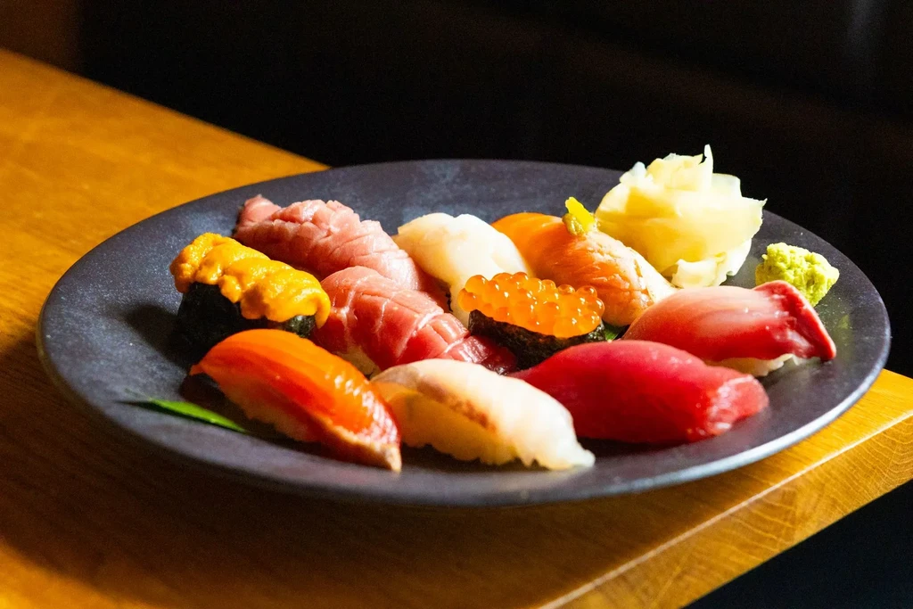 Assortment of fresh sushi and nigiri with ginger and wasabi on dark plate.