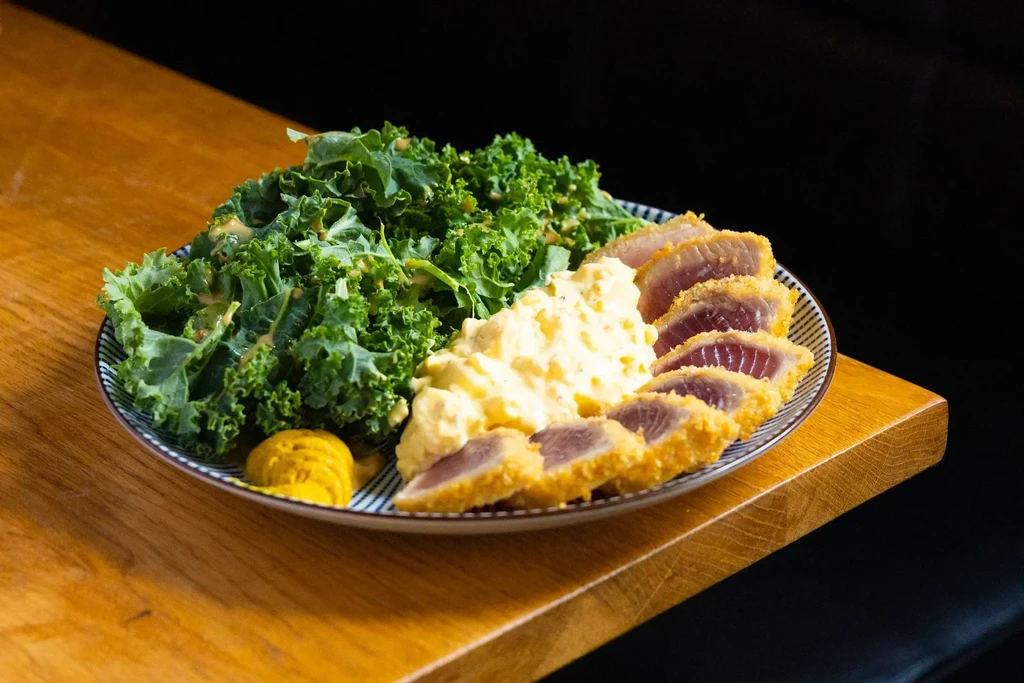 Seared rare tuna, green kale, creamy salad, and mustard on a plate.
