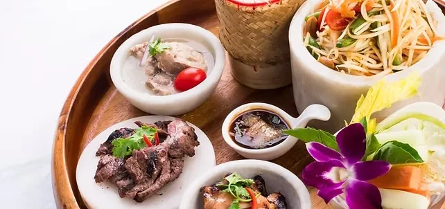 Beautifully arranged Thai meal on a wooden tray with papaya salad.