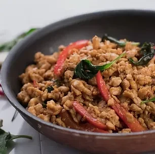 Stir-fried minced meat with red chilies and basil in a dark pan.