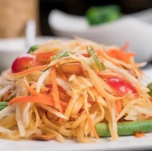 Vibrant close-up of Thai papaya salad with tomatoes and green beans.