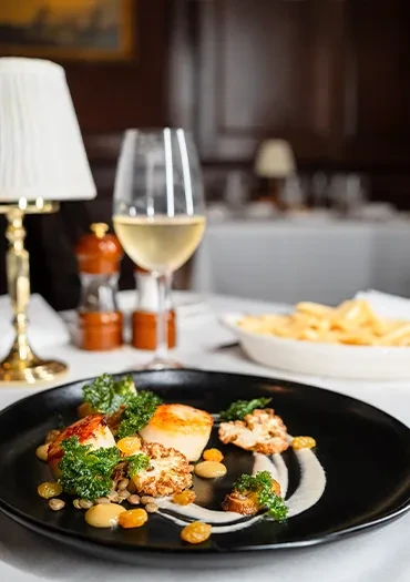 Artfully plated scallops, cauliflower, and lentils on a black dish.