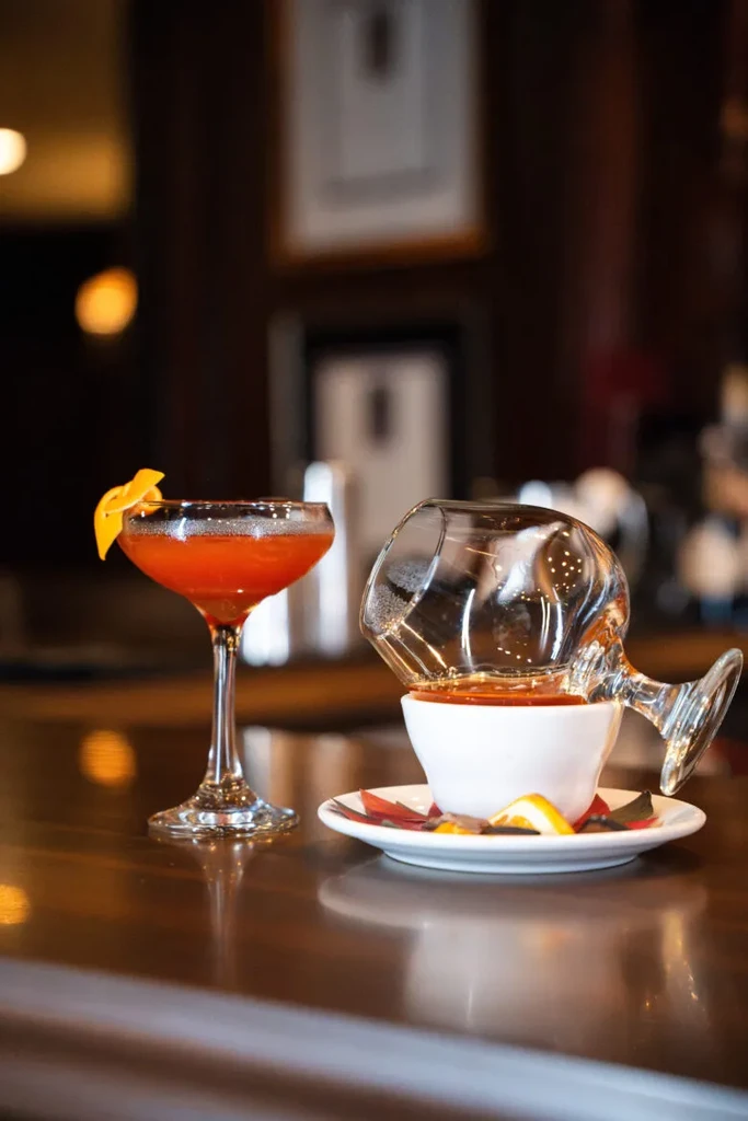 Two elaborate cocktails: one in a coupe, one inverted over a teacup.
