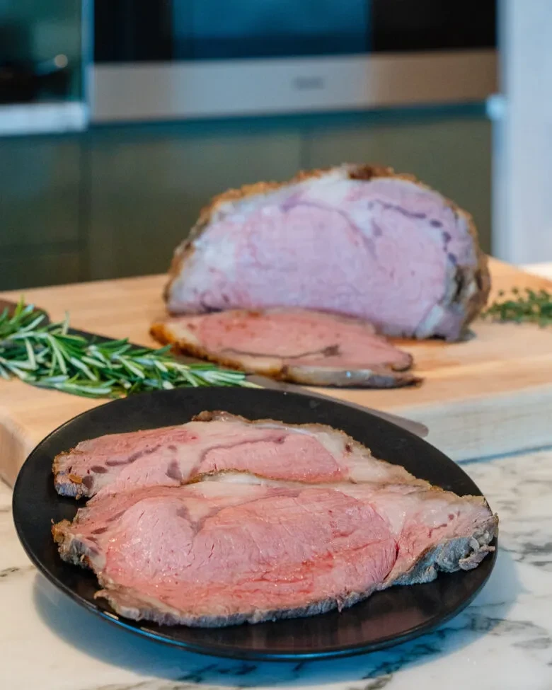 Medium-rare roast beef, carved on a board with rosemary and thyme.