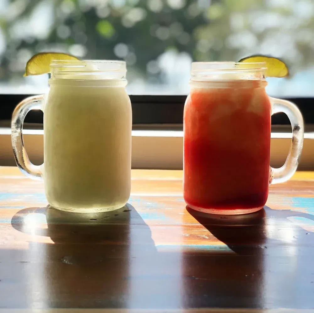 Two lime-garnished drinks in mason jars on a wooden table.