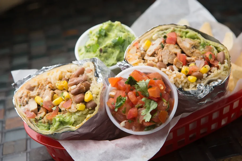 Two halved burritos filled with meat, rice, guacamole, served with salsa.