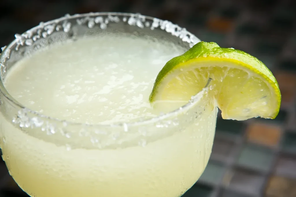 Frozen yellow drink in stemmed glass, salted rim, lime wedge.