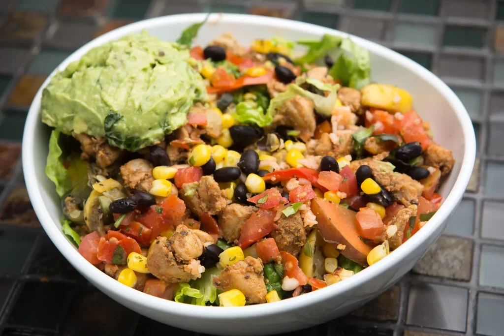 Colorful burrito bowl with chicken, greens, beans, corn, and guacamole.