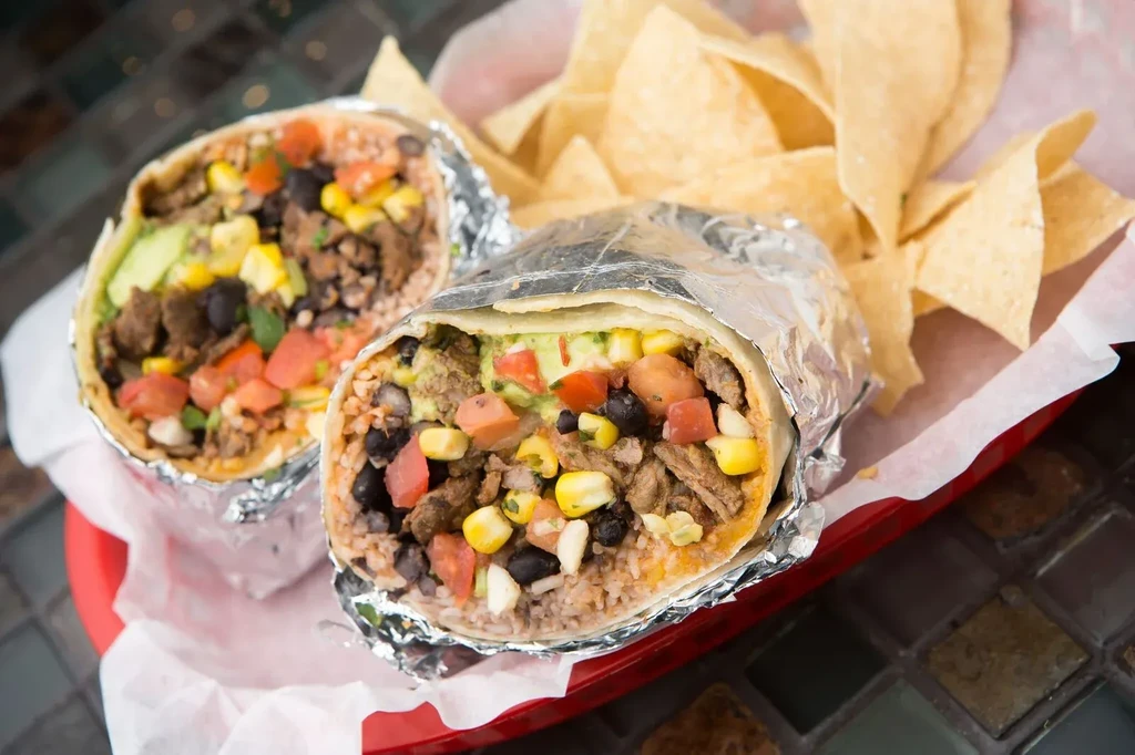 Two sliced burritos with visible fillings and chips in a red basket.