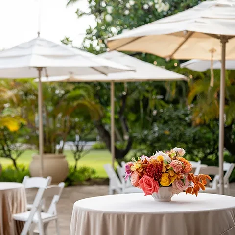 Outdoor dining table with vibrant floral centerpiece and umbrellas.