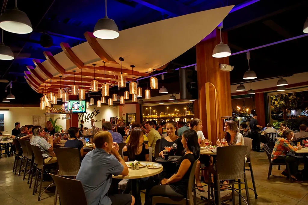 Bustling Nico's AT NIGHT restaurant, blue uplighting, city view, smiling server.