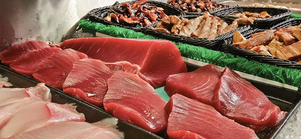 Fresh raw red tuna fillets and other fish at a seafood counter.