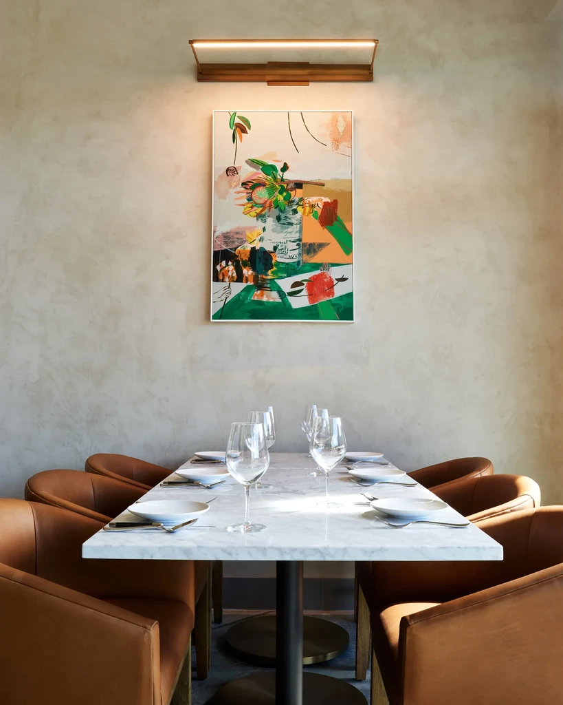 Meticulously set marble dining table, leather chairs, and colorful abstract art.