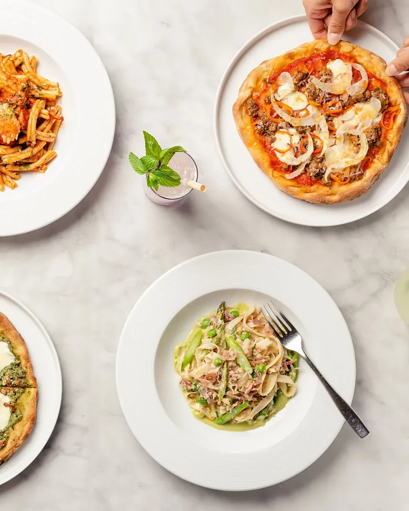 Overhead shot of pasta, pizzas, and a drink on a marble table.