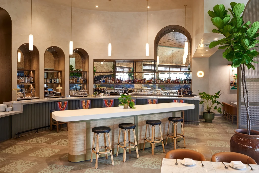 Contemporary bar interior with white oval counter, rattan stools, liquor bottles.