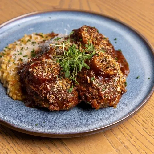 Braised meat with crispy topping, creamy risotto, and herbs on blue plate.