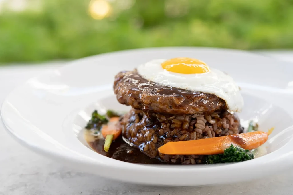 Loco moco with sunny-side egg, meat patty, rice, gravy, carrots, broccoli.