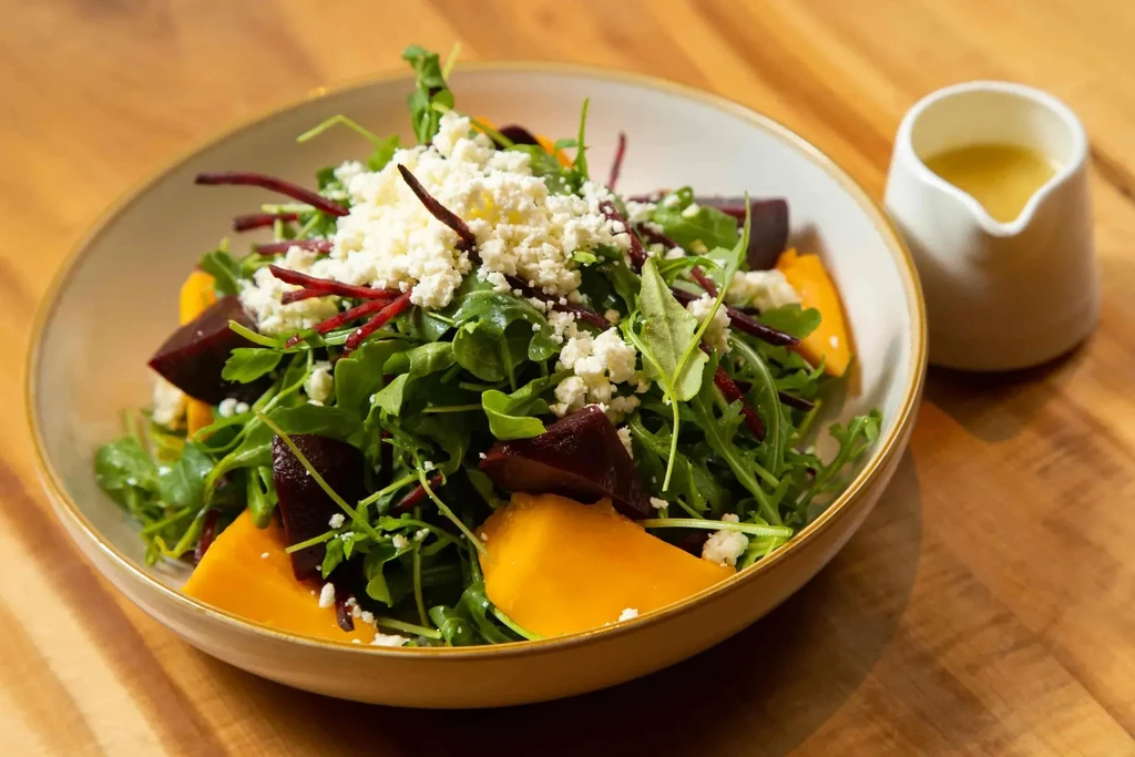 Vibrant salad with beets, greens, crumbled cheese, and dressing.