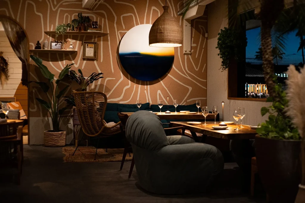 Warm restaurant interior with circular art, plants, and diverse seating.