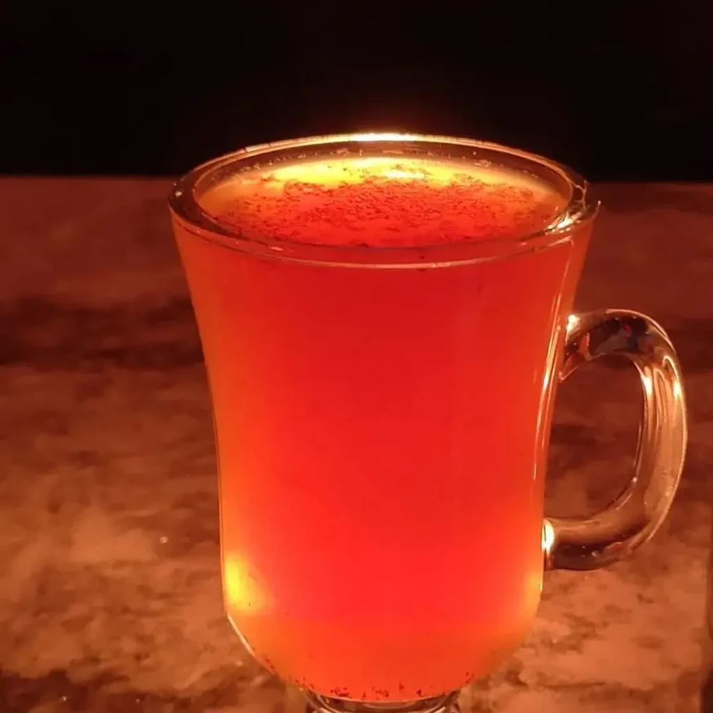 Glowing orange drink in a clear glass mug with dark powder.