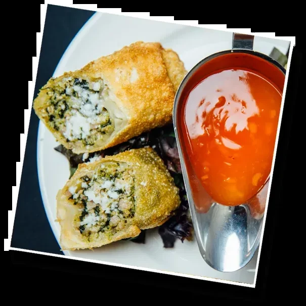 Close-up: Two golden fried rolls, cut, with savory filling and orange sauce.