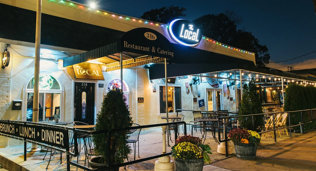 The Local restaurant exterior at night with neon sign and lit patio.