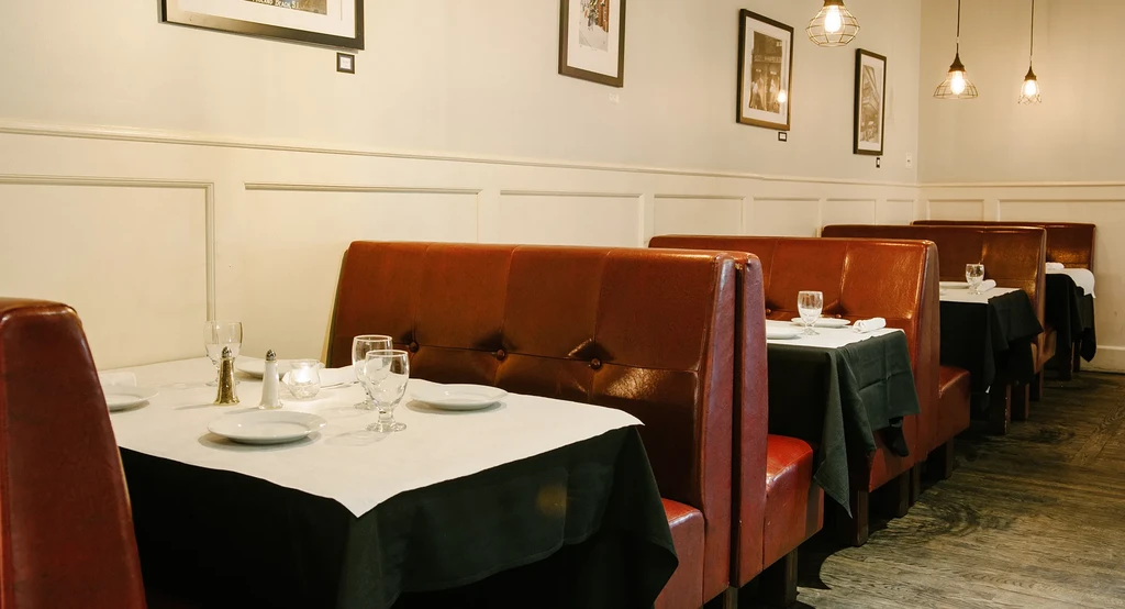 Restaurant interior with empty reddish-brown booths and fully set tables.