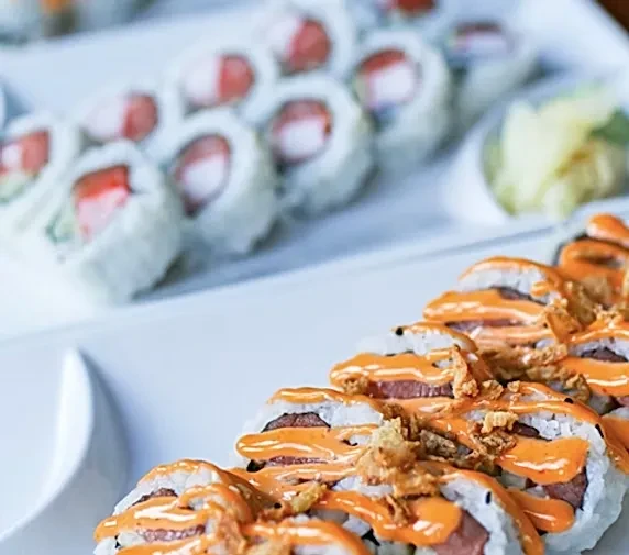 Two plates of sushi rolls, one with orange sauce and fried onions.