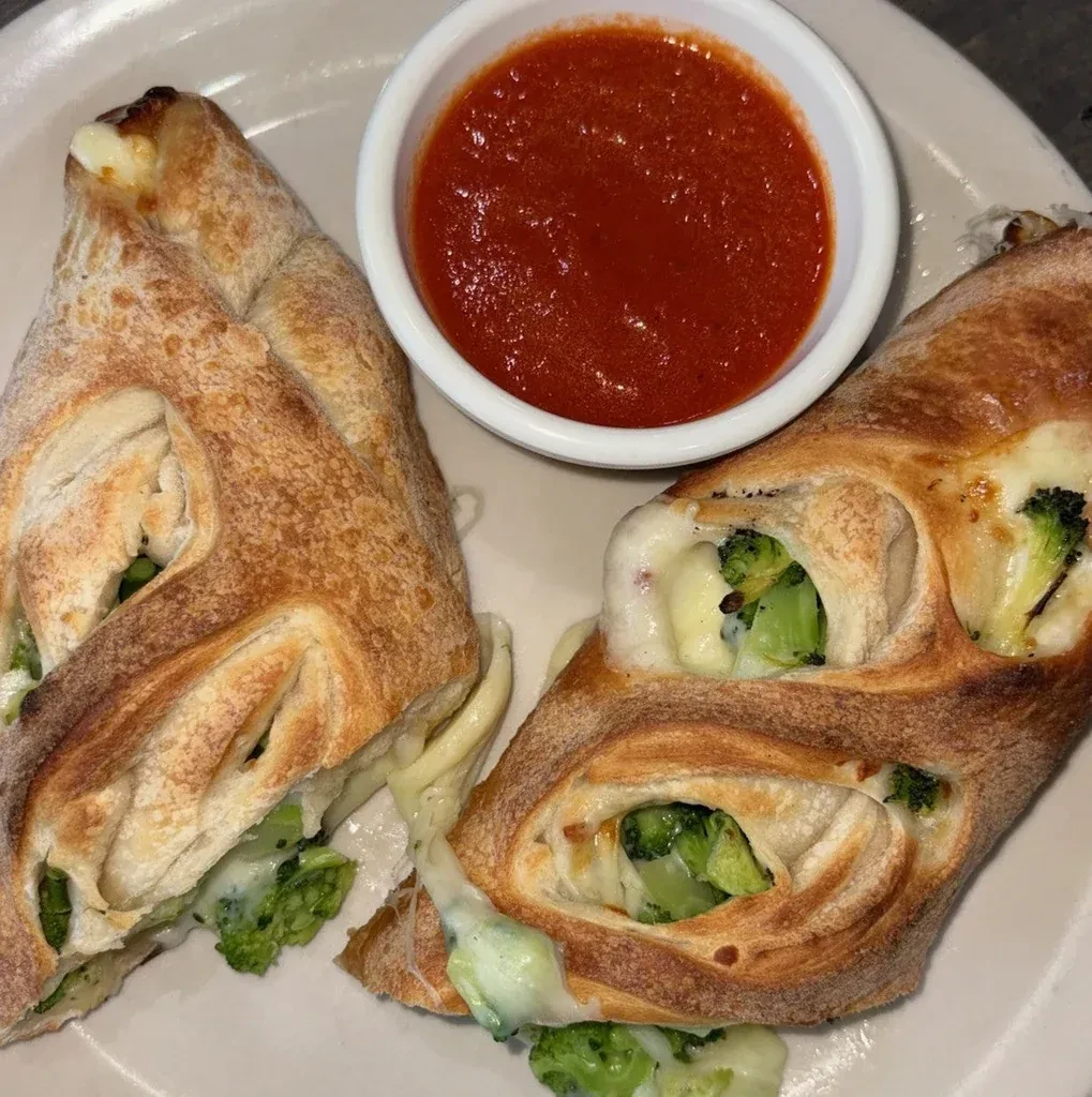 Two broccoli and cheese strombolis with a side of marinara sauce.