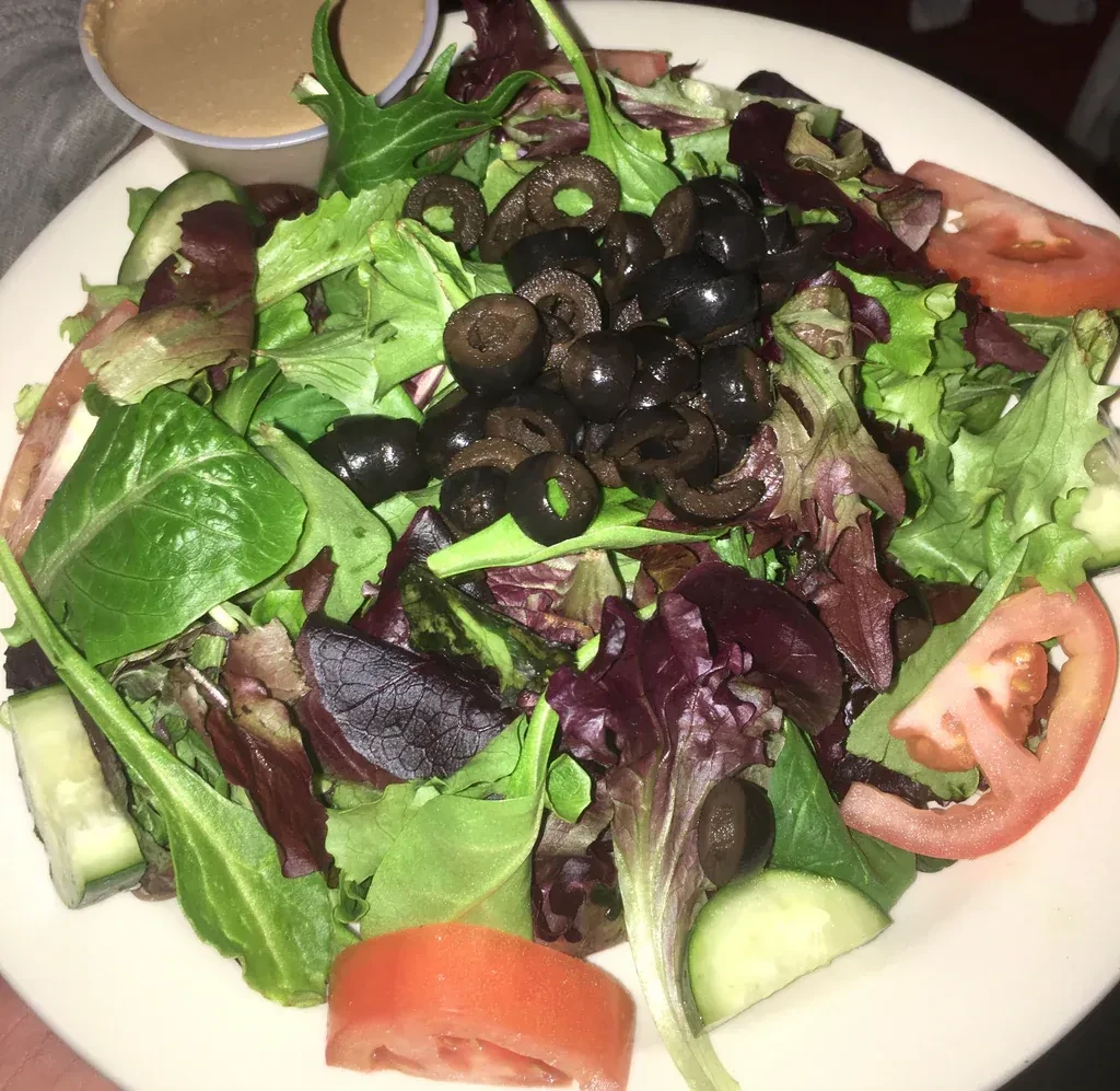 A fresh side salad with lettuce, tomato, cucumber, black olives, and dressing.