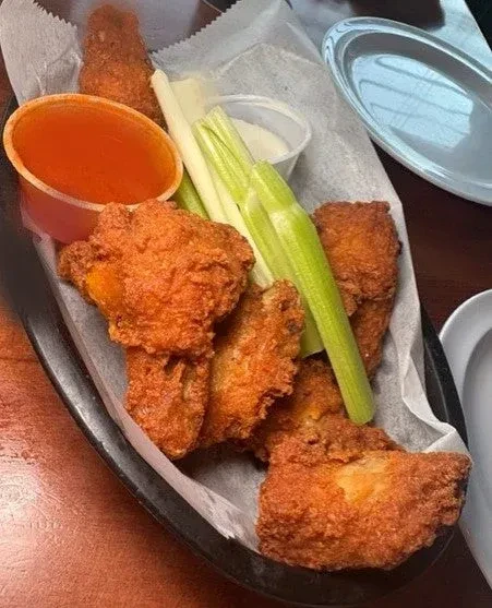 Fried chicken wings with celery sticks and dipping sauces in a basket.