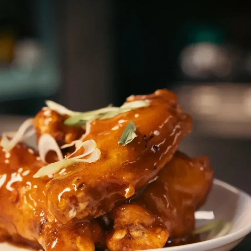 Close-up of glazed chicken wings with sesame seeds and green onions.
