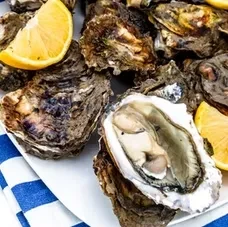 A plate of oysters, one open, with lemon wedges and a blue napkin.