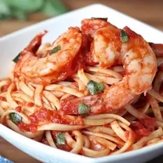 Shrimp scampi with linguine, tomato sauce, and basil in a white bowl.
