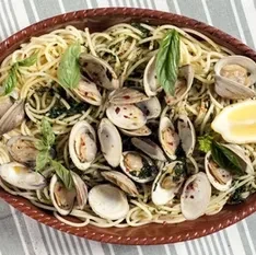 Spaghetti with clams, basil, and lemon wedge in a brown ceramic dish.