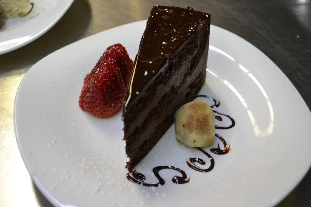 A slice of chocolate cake with strawberry and fig on a white plate.