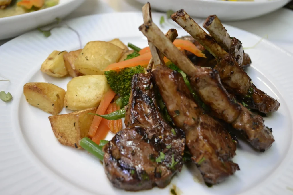 Plate of grilled lamb chops with roasted potatoes and steamed vegetables.