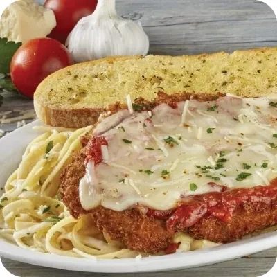 Close-up of chicken parmesan, pasta, garlic bread, and fresh ingredients.