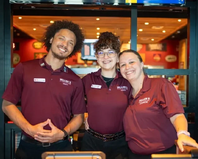Three smiling Miller's Alehouse Coaches in maroon polo shirts.