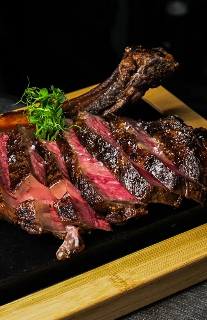 A sliced, medium-rare tomahawk steak with herbs on a wooden board.