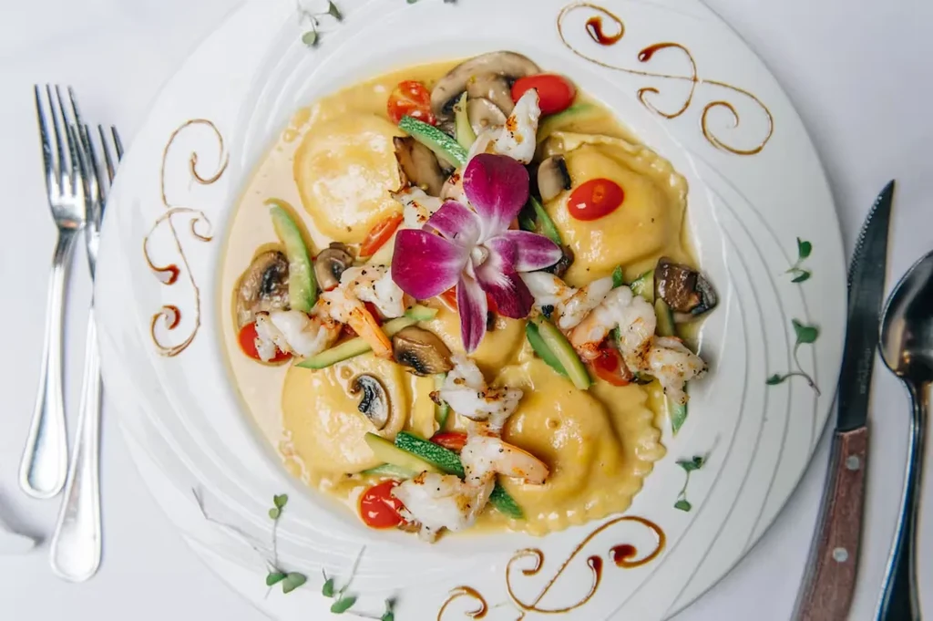 Ravioli with shrimp, mushrooms, and vegetables, garnished with an orchid.