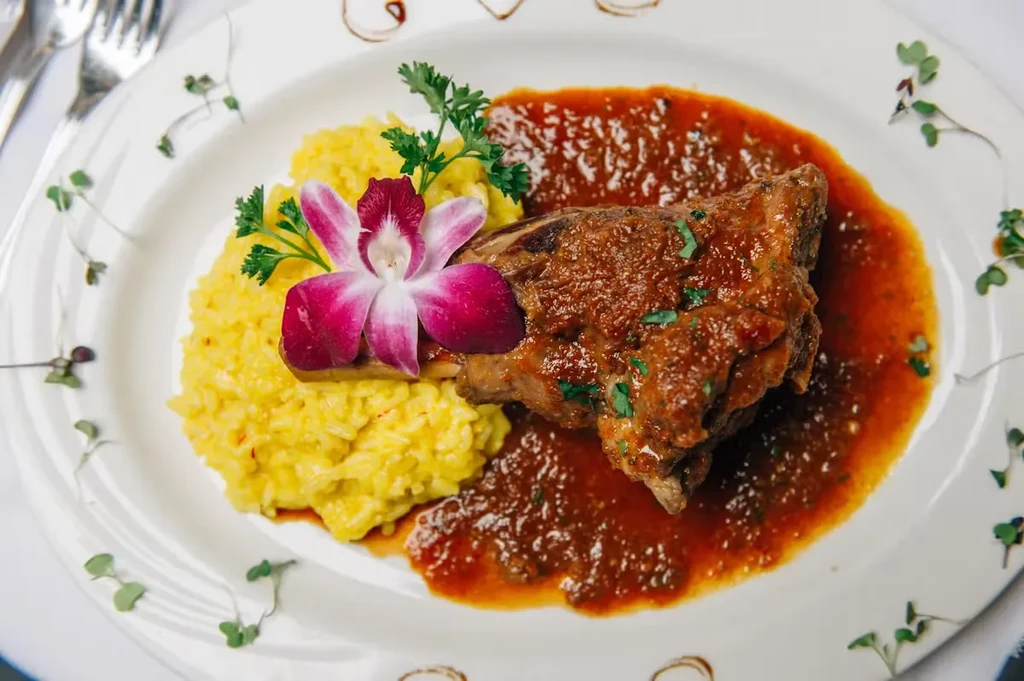 Braised short rib in red sauce with yellow risotto and an orchid garnish.