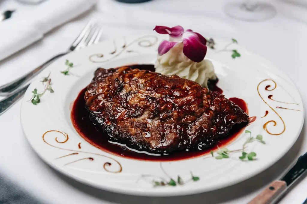 Glazed steak with mashed potatoes, garnished with a purple orchid.