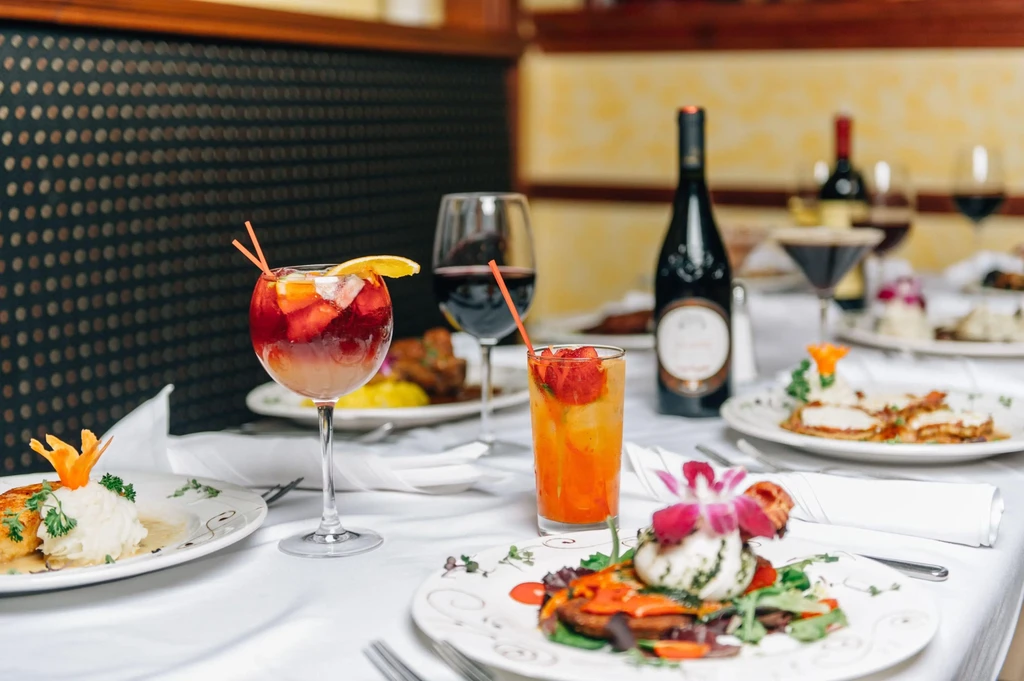Restaurant table set with drinks, plates of food, and wine bottles.