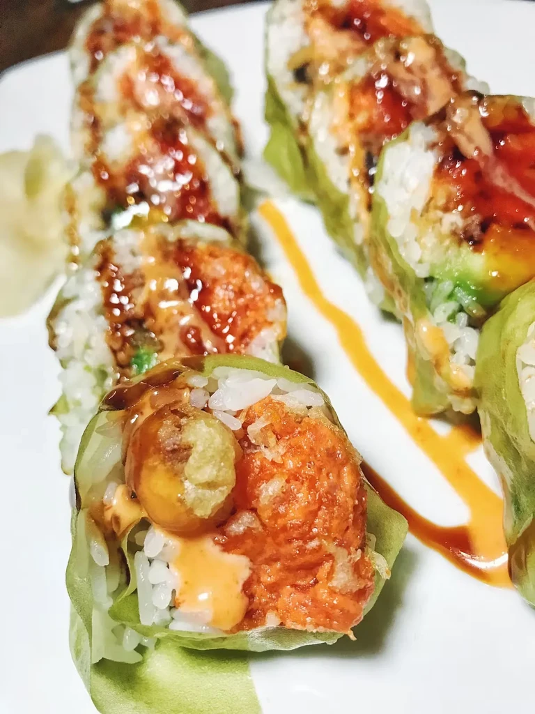 Six sushi rolls with orange sauce and green wraps on a white plate.