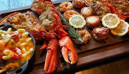 A platter of cooked lobster, shrimp, scallops, lemon, and macaroni.