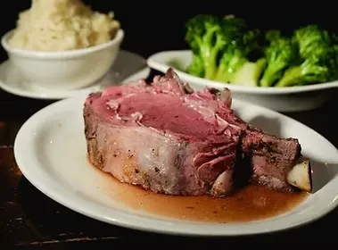 A thick slice of rare prime rib with mashed potatoes and broccoli.